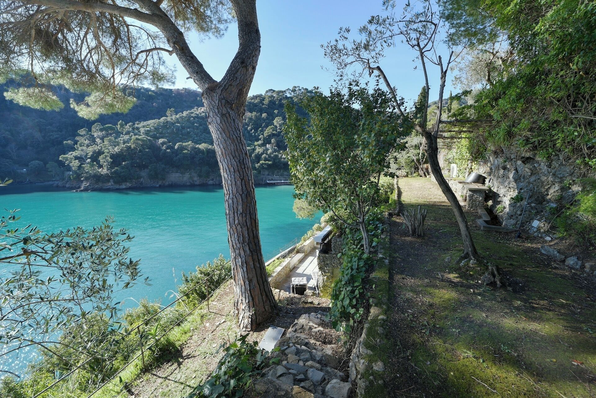 Un paisaje costero con un camino de piedra que lleva a un banco con vistas a aguas turquesas.