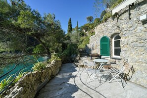 A stone building with a stone staircase, outdoor seating, and a view of a body of water. - The Stone Pine House - Paraggi (Santa Margherita Ligure)