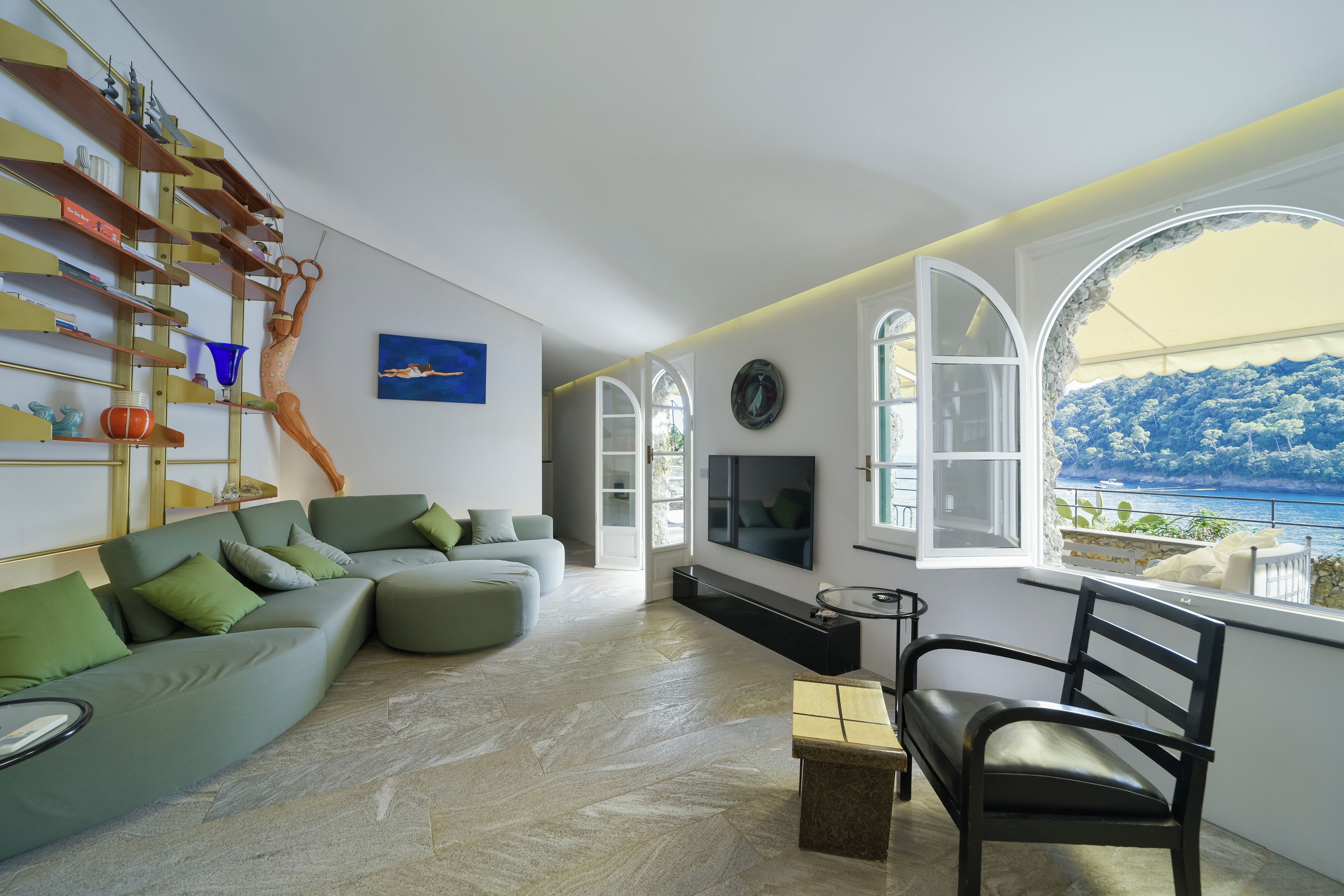 Un salon moderne avec un canapé d’angle, un téléviseur et une vue sur la mer.