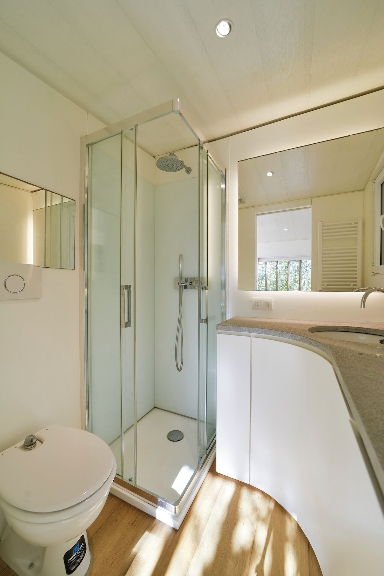 Une salle de bain moderne avec une douche à parois de verre, des toilettes blanches et un meuble-lavabo avec un miroir.