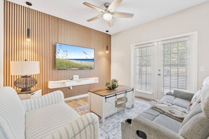 Ein Wohnzimmer mit Fernseher, Deckenventilator, Holzpaneelen, einem Fenster mit Jalousien und einem Sofa.