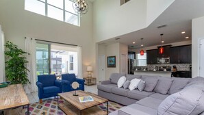 A spacious living area with a gray sofa, blue armchairs, a wooden coffee table, and a colorful rug. - Modern 5BR Oasis Near Disney - Pvt pool - 4712SL (Kissimmee)