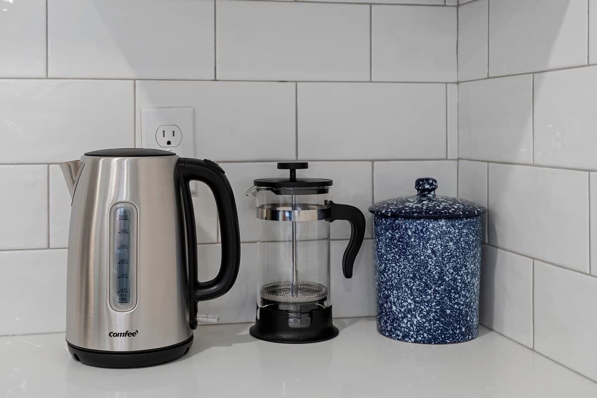 Una cucina con una macchina da caffè in acciaio inox, un bollitore a stantuffo e un contenitore di ceramica blu.