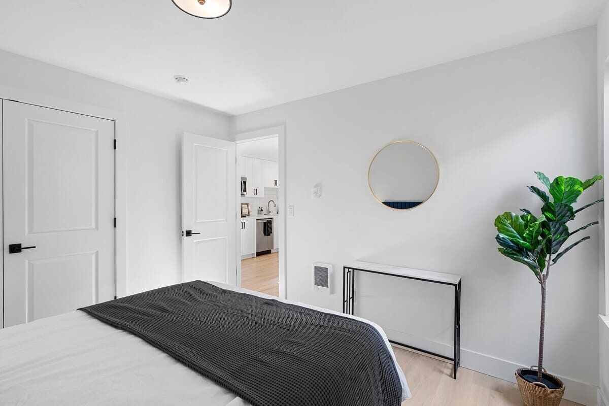 A bedroom with a bed, a bedside table, a mirror, and a potted plant.