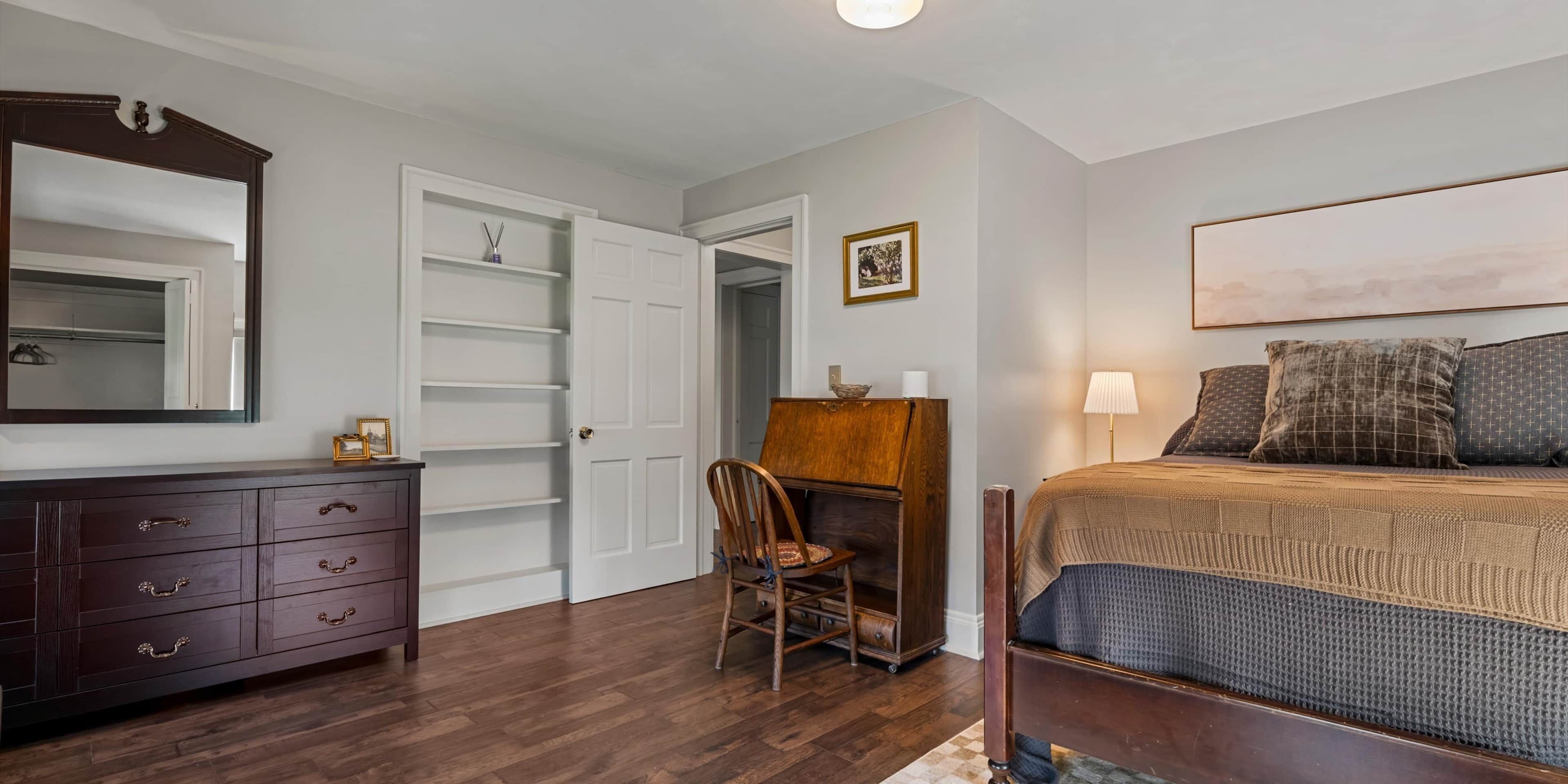A bedroom with a bed, a dresser, a chair, a wardrobe, and a door.
