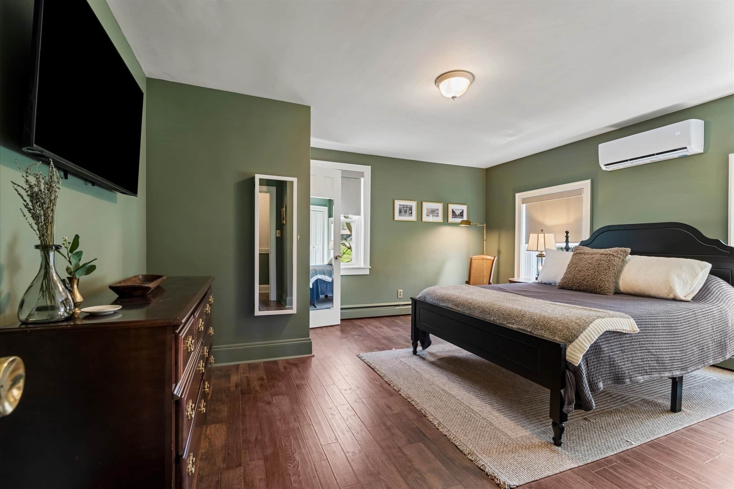 Une chambre à coucher comprenant un lit, une commode, un miroir et un appareil de climatisation fixé au mur.