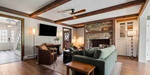Ein Wohnzimmer mit Kamin, Fernseher, Sofa, Couchtisch und einem Sessel.