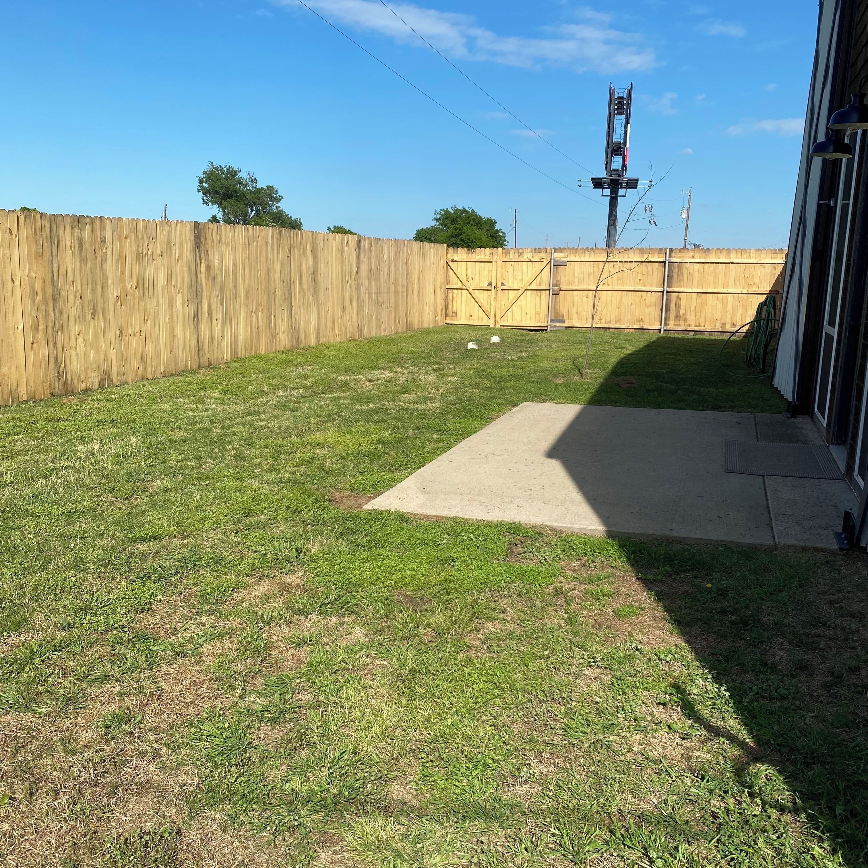 A backyard with a wooden fence, a concrete patio, and a grassy area.