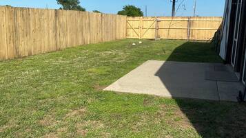 A backyard with a wooden fence, a concrete patio, and a grassy area.