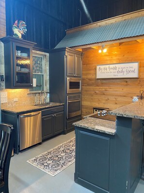 Une cuisine moderne avec des meubles de couleur sombre, des appareils électroménagers en acier inoxydable et un coq décoratif.