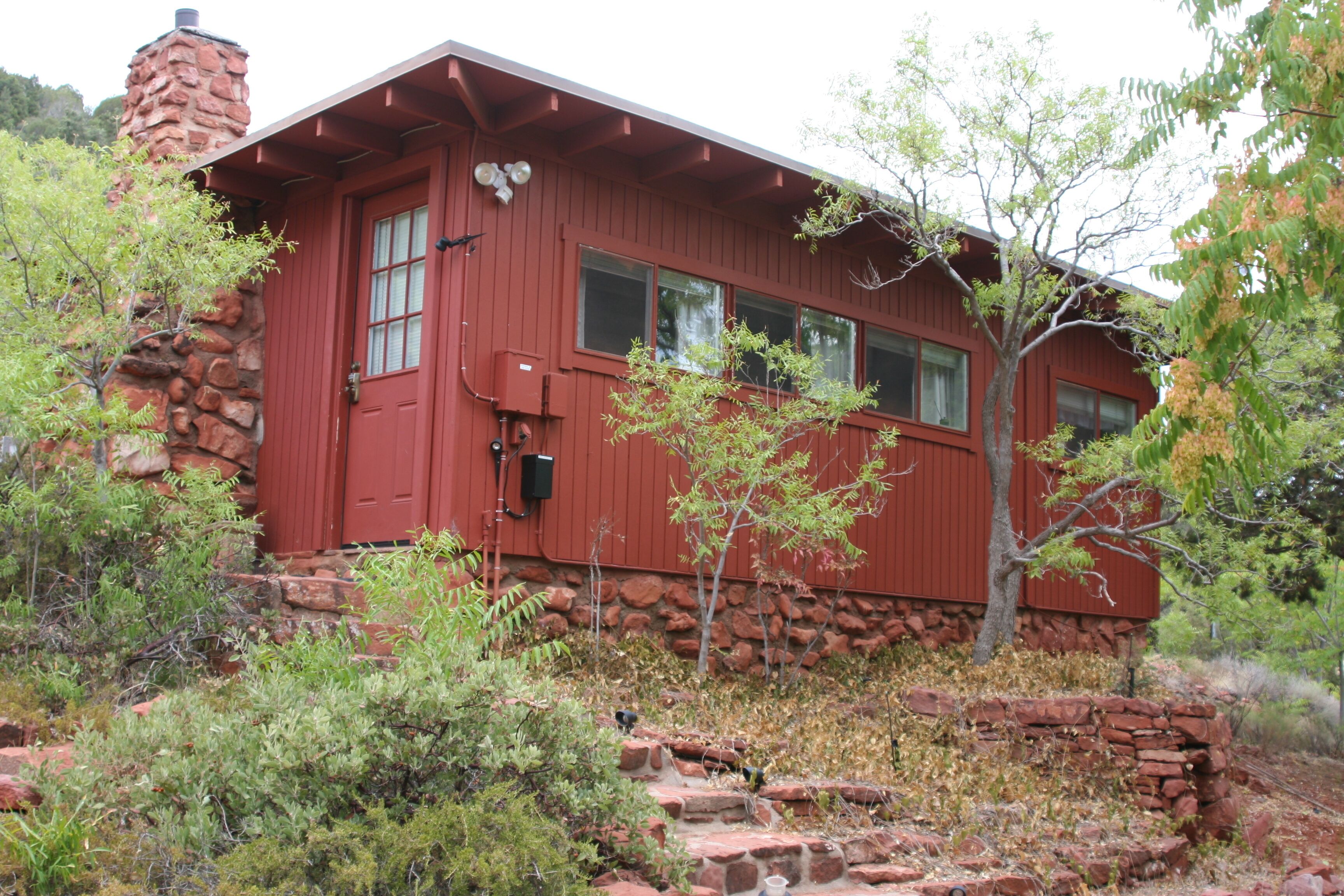 A red wooden cabin with a stone chimney, windows, and a small porch area.