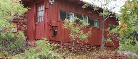 A red wooden cabin with a stone chimney, windows, and a small porch area.