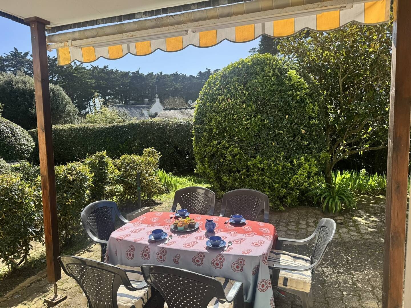 An outdoor patio with a table set for four, surrounded by chairs, under a striped awning.