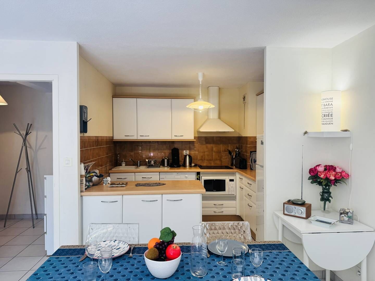 Een kleine keuken met witte kastjes, een magnetron, en een eethoek met een tafel gedekt voor twee personen.