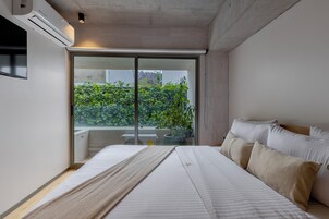 A modern bedroom with a large bed, a sliding glass door to a balcony, and an air conditioning unit on the wall.