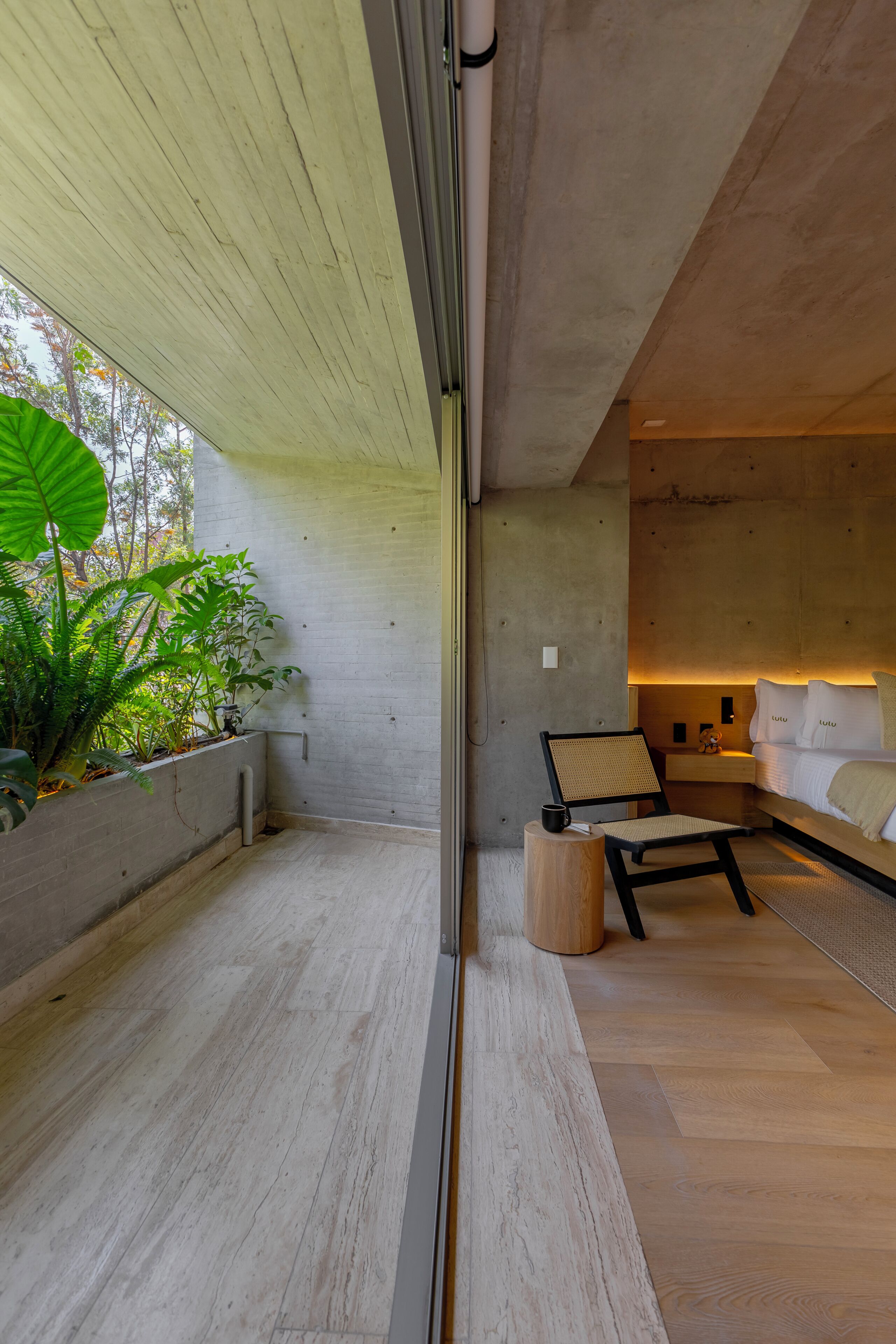 Une chambre moderne avec un mur en béton, un plancher en bois, un lit avec une literie blanche, une chaise et une petite table.