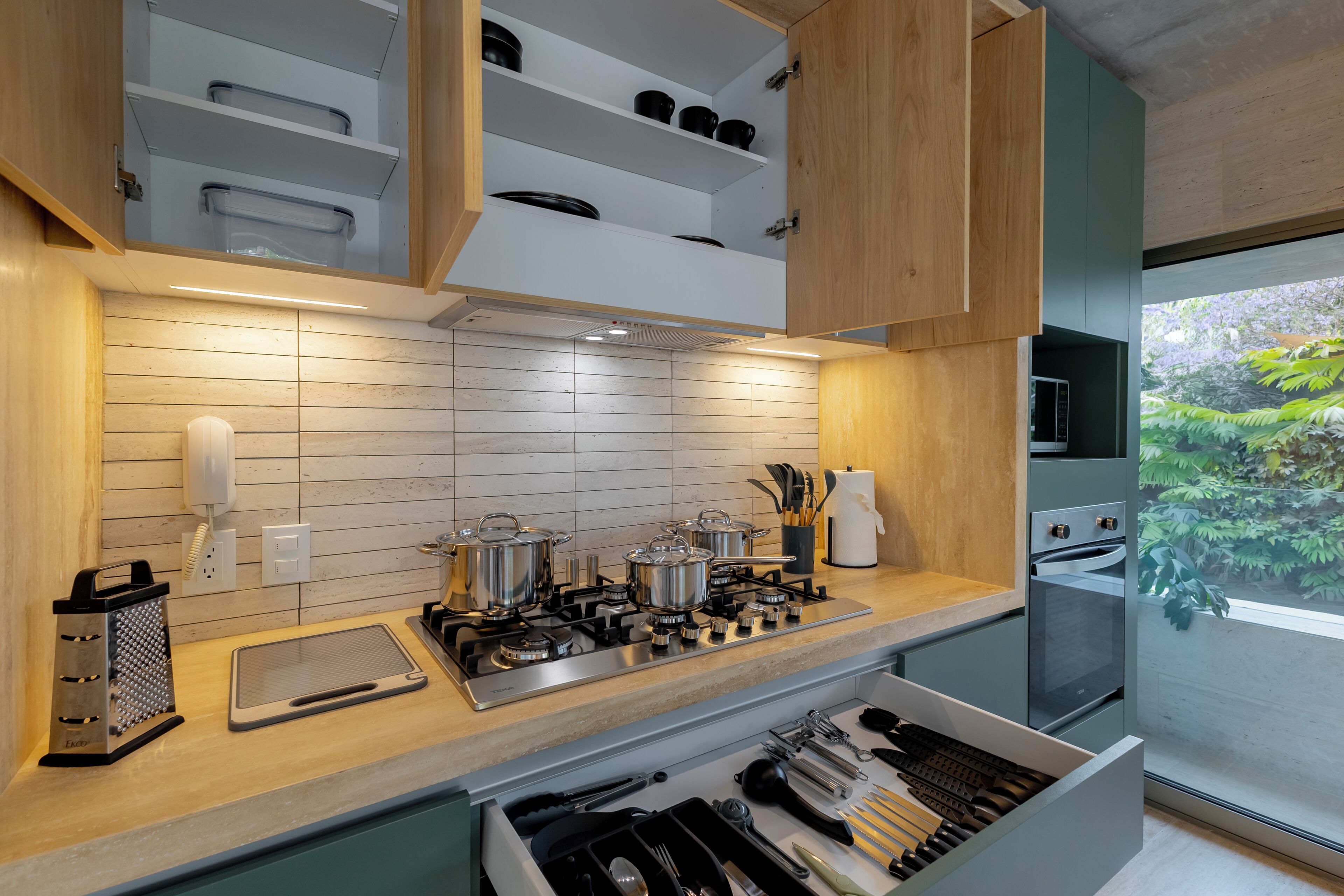 Een moderne keuken met een ingebouwde kookplaat, bovenkasten en uitzicht op groen.