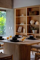 Una mesa de comedor de madera con cuencos negros y vasos de jugo de naranja, rodeada de sillas de mimbre.