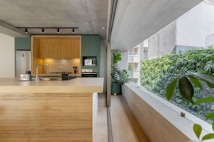 A modern kitchen with wooden cabinets, a stainless steel sink, and a view of a balcony with greenery.