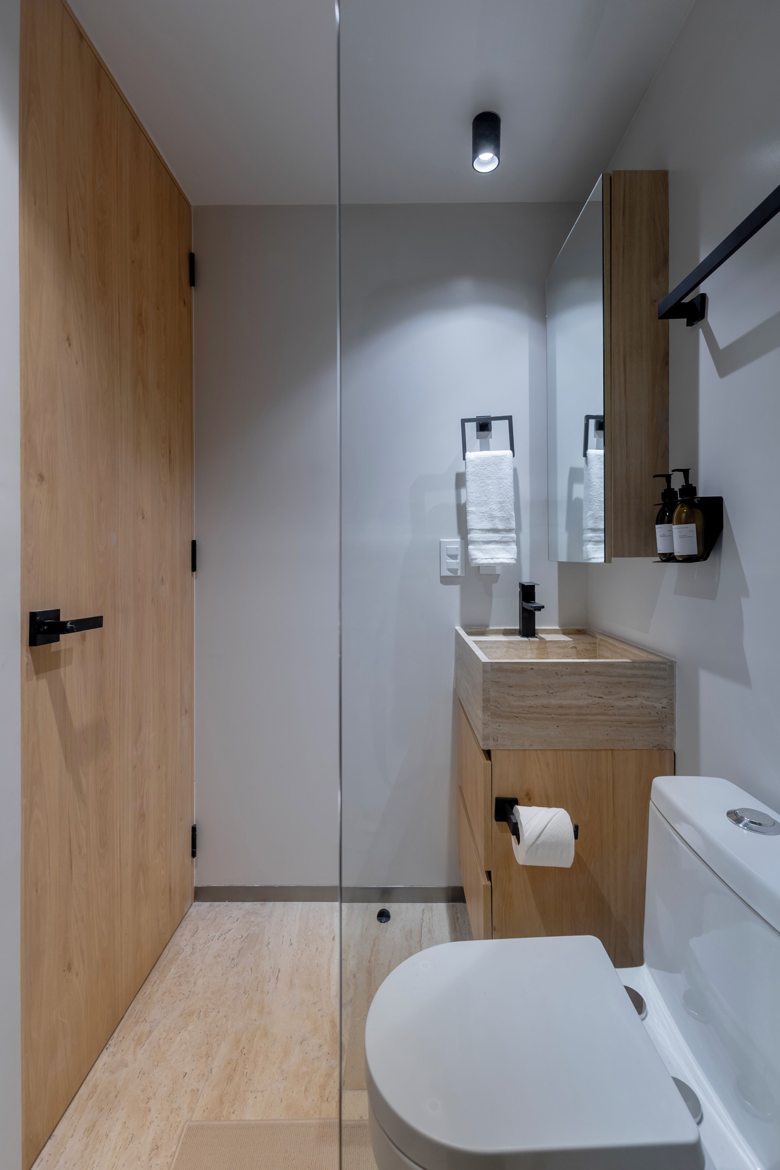 A modern bathroom with a glass shower enclosure, a wooden vanity, and a white toilet.