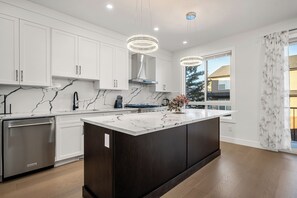 Una cocina moderna con armarios blancos, encimera de mármol, una isla central e iluminación colgante.