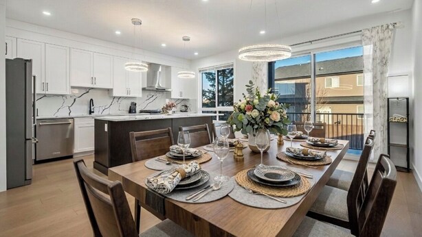 Una cocina moderna con armarios blancos, una mesa de comedor lista para seis comensales y un gran ventanal con vistas a edificios.