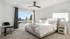 Un dormitorio con cama, una silla, una mesita de noche, un ventilador de techo y una ventana.