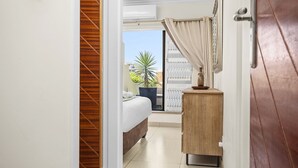 Ein Hotelzimmer mit einem Bett, einem Holzschrank, einer Topfpflanze und einer Glastür, die auf einen Balkon mit einer Palme führt.