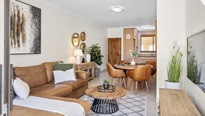 Ein Wohnzimmer mit einem braunen Ledersofa, einem runden Holztisch, einem Essbereich mit Holztisch und Stühlen sowie einer Küche im Hintergrund.