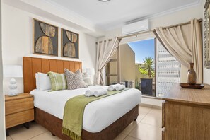 Une chambre d’hôtel avec un lit, une table de chevet, un bureau, une fenêtre avec des rideaux et des œuvres d’art accrochées au mur.