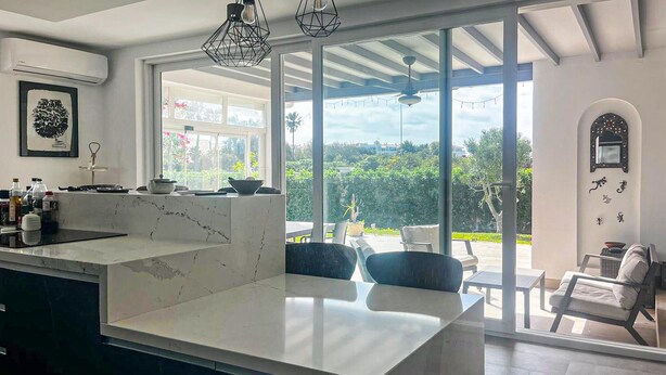 A modern kitchen with a large island, large windows, and a view of the outdoors.