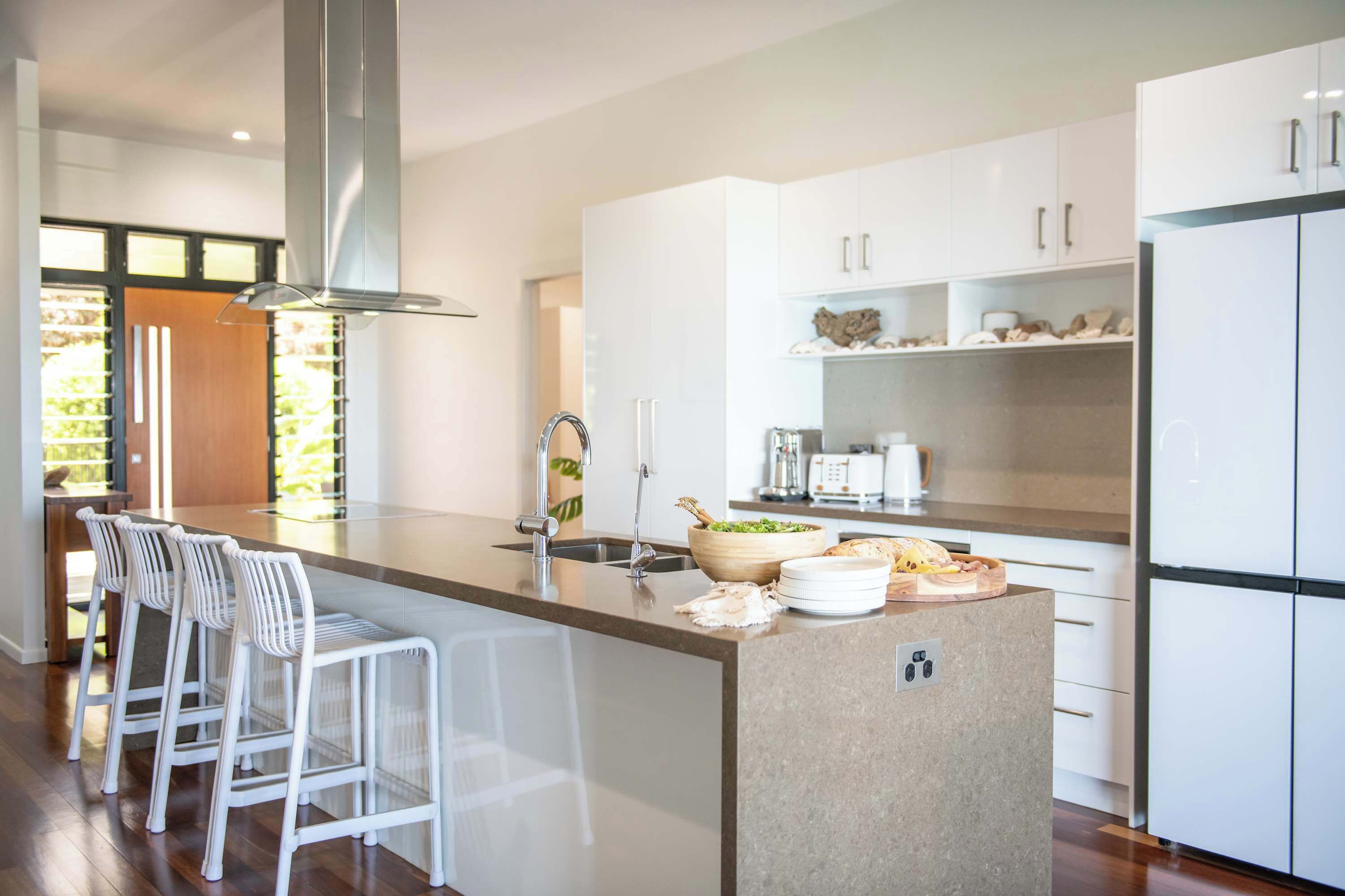 A modern kitchen with white cabinetry, a central island with bar stools, and a stainless steel range hood.