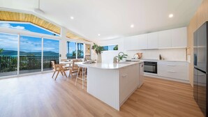 Une cuisine moderne dotée d’un îlot central, de meubles blancs et offrant une vue sur l’extérieur.