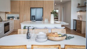 Une cuisine moderne avec des meubles en bois, un îlot central doté d’un évier et un coin repas avec une table ronde et des chaises.