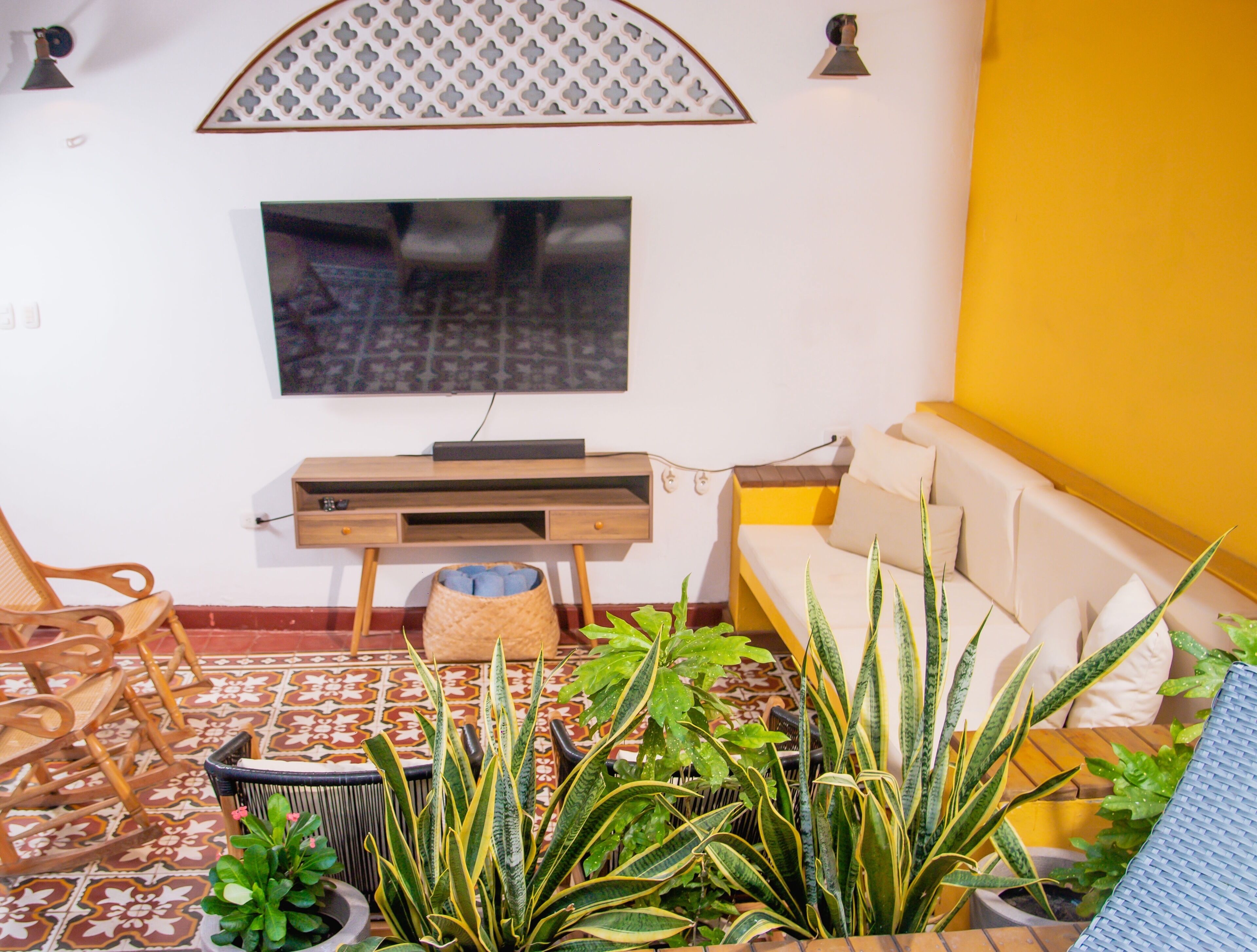 Ein Wohnzimmer mit Fernseher, Sofa, Sesseln und Topfpflanzen.