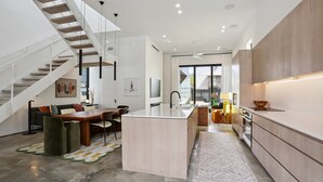 A modern kitchen with a central island, a dining area with a wooden table and chairs, and a staircase leading to another level. - Modern House, walk to French Quarter or the street car is a block away! (New Orleans)