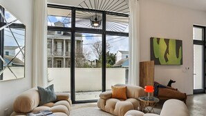 A modern living room with large windows, a sofa, a coffee table, and a painting on the wall. - Modern House, walk to French Quarter or the street car is a block away! (New Orleans)