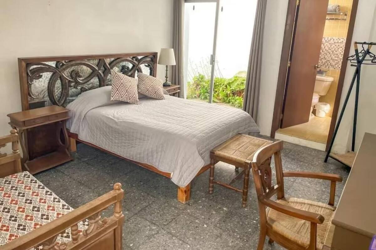Un dormitorio con cama, una silla, una mesita de noche y vistas al exterior.