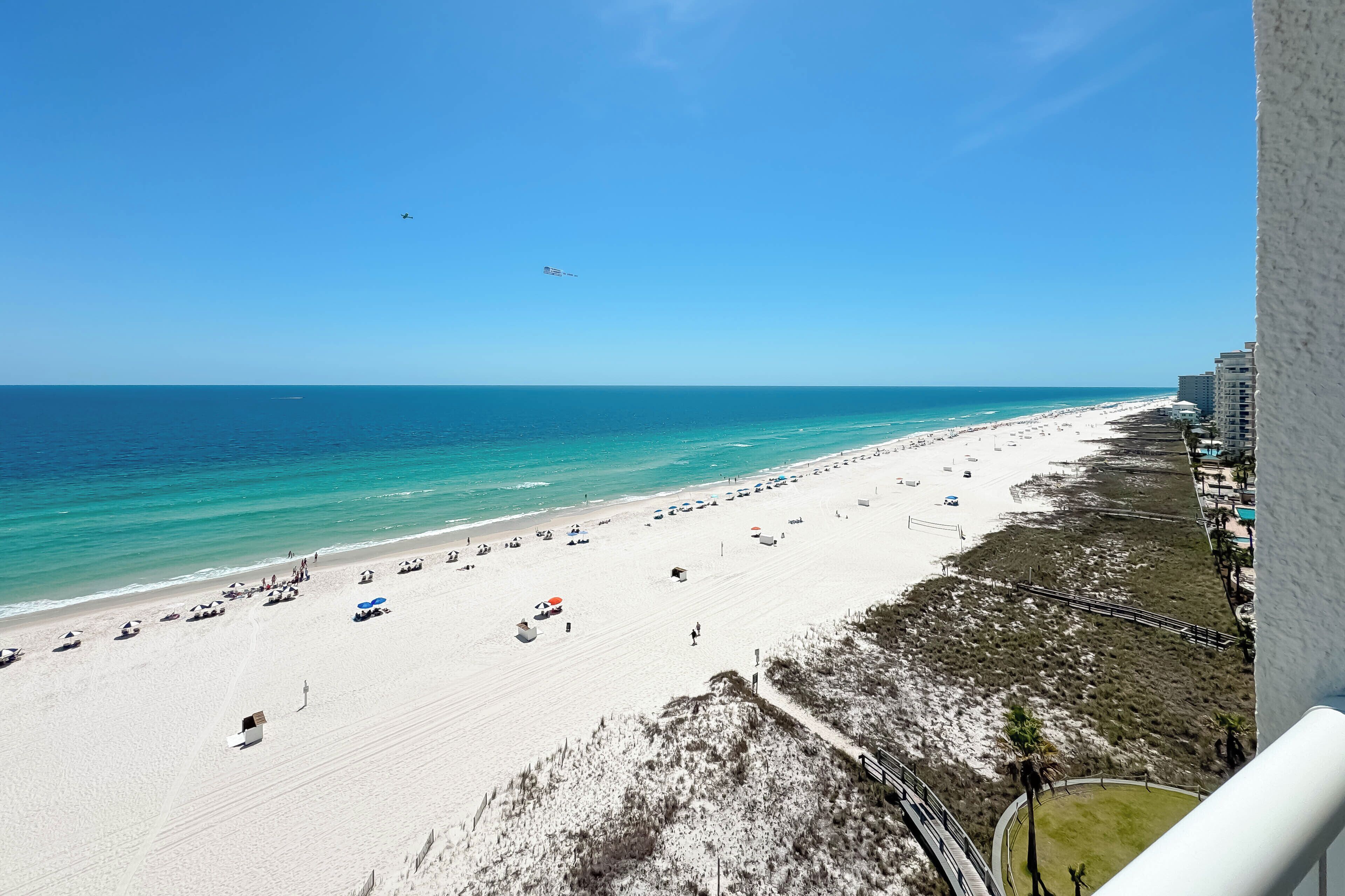 Blick auf einen Strand mit blauem Himmel, Sand und einigen Sonnenschirmen.