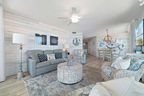 A living room with a sofa, round coffee table, and a dining area with a table and chairs. - Summer House 1101B | Beachfront Condo | Resort Amenities | Indoor & Outdoor Pool | My Beach Getaways (Orange Beach)