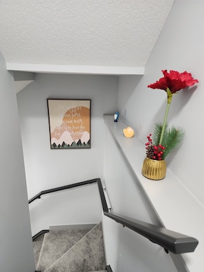 Een trap met een leuning, een lijst met een motiverende quote, een rode bloem en een klein decoratief object op een plank.