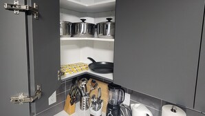 Een kleine keuken met grijze kastjes, een aanrecht en diverse keukengerei en pannen.