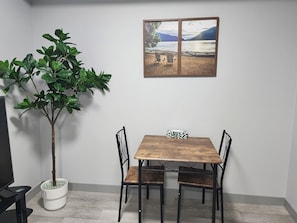 Een eetgedeelte met een houten tafel, vier stoelen, een plant in pot en een lijst met een foto van een meer.