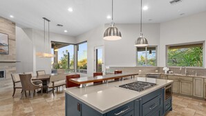 Una cucina moderna con un'isola grande, illuminazione a sospensione e vista su piante verdi.
