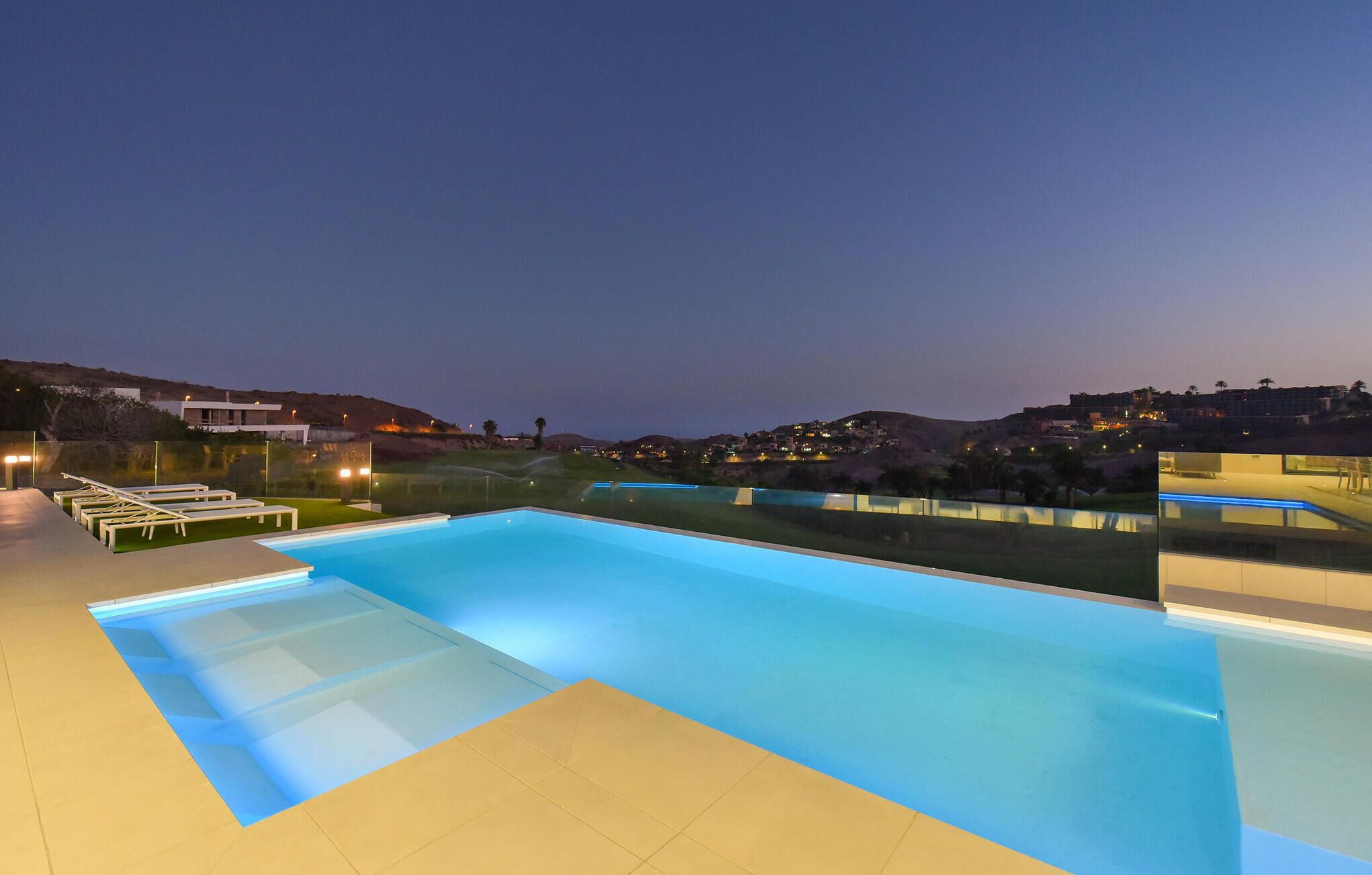 A swimming pool with lounge chairs and a view of a hillside at dusk.