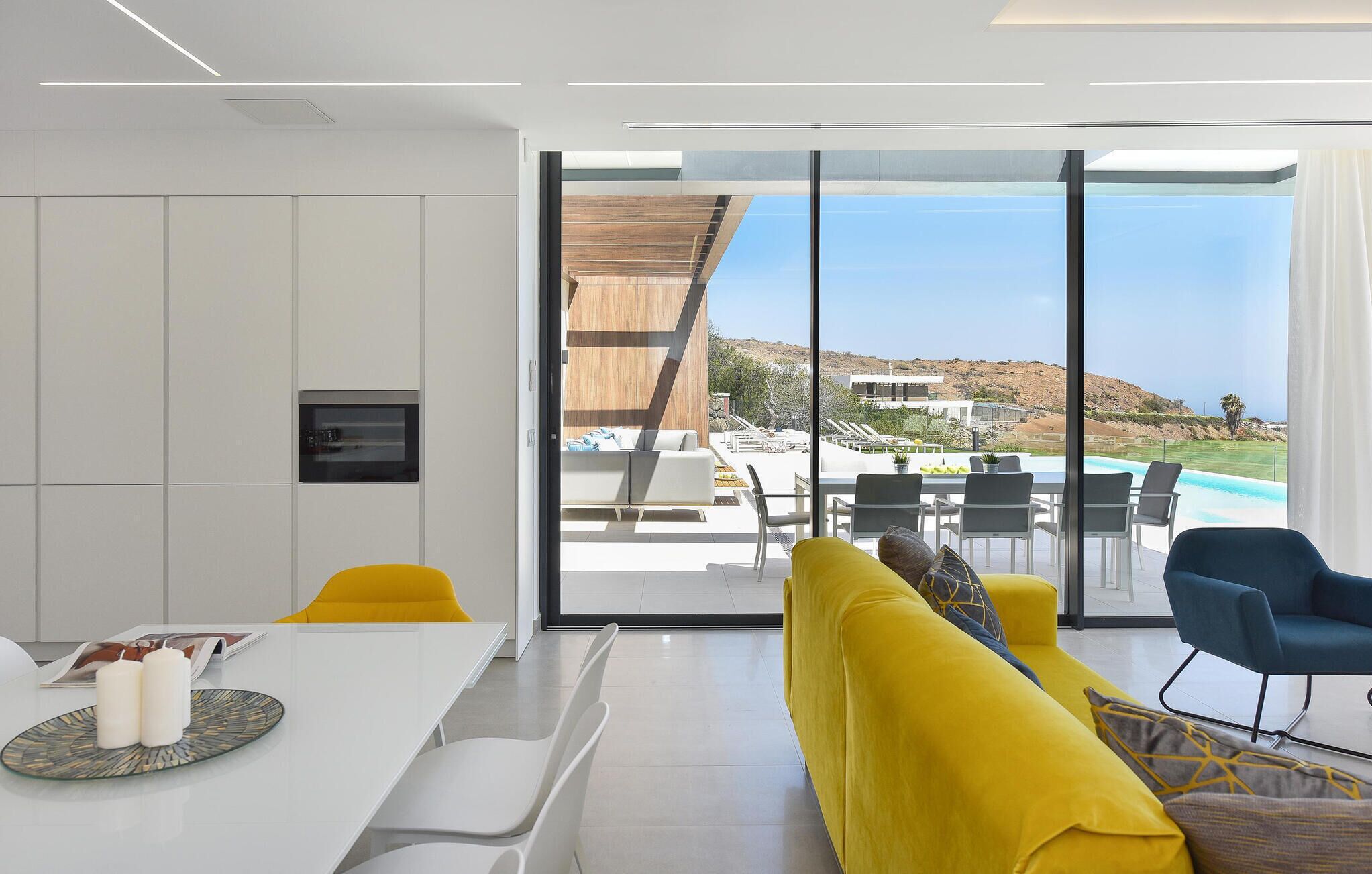 Ein modernes Wohnzimmer mit einem großen Schiebeglasfenster, das zu einem Außenbereich mit Pool und Blick auf Hügel führt.