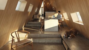 Ein modernes Interieur mit Holzbalkendecken, einer Holzbank, einem Tisch und einem Hund, der auf einer Ablage liegt.
