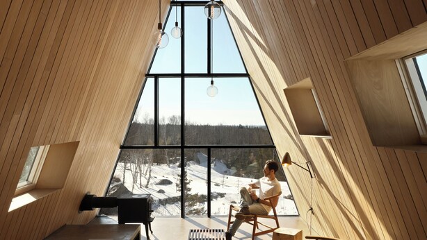 Ein modernes Interieur mit Holz-Schrägdecken, großen Fenstern und einer Sitzecke mit Tisch und Stühlen.