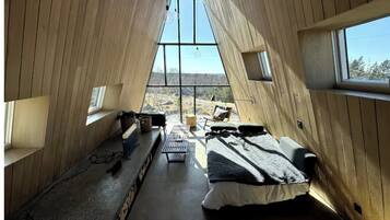 Een kamer met een schuine kap, grote ramen, een bed, een bureau en uitzicht op het landschap.