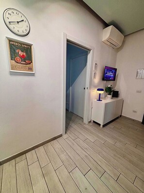 A hallway with a clock, a poster, a television, and a door leading to another room. - Quiet One-Bedroom Apartment 80 m from the M1 Metro (Milano)